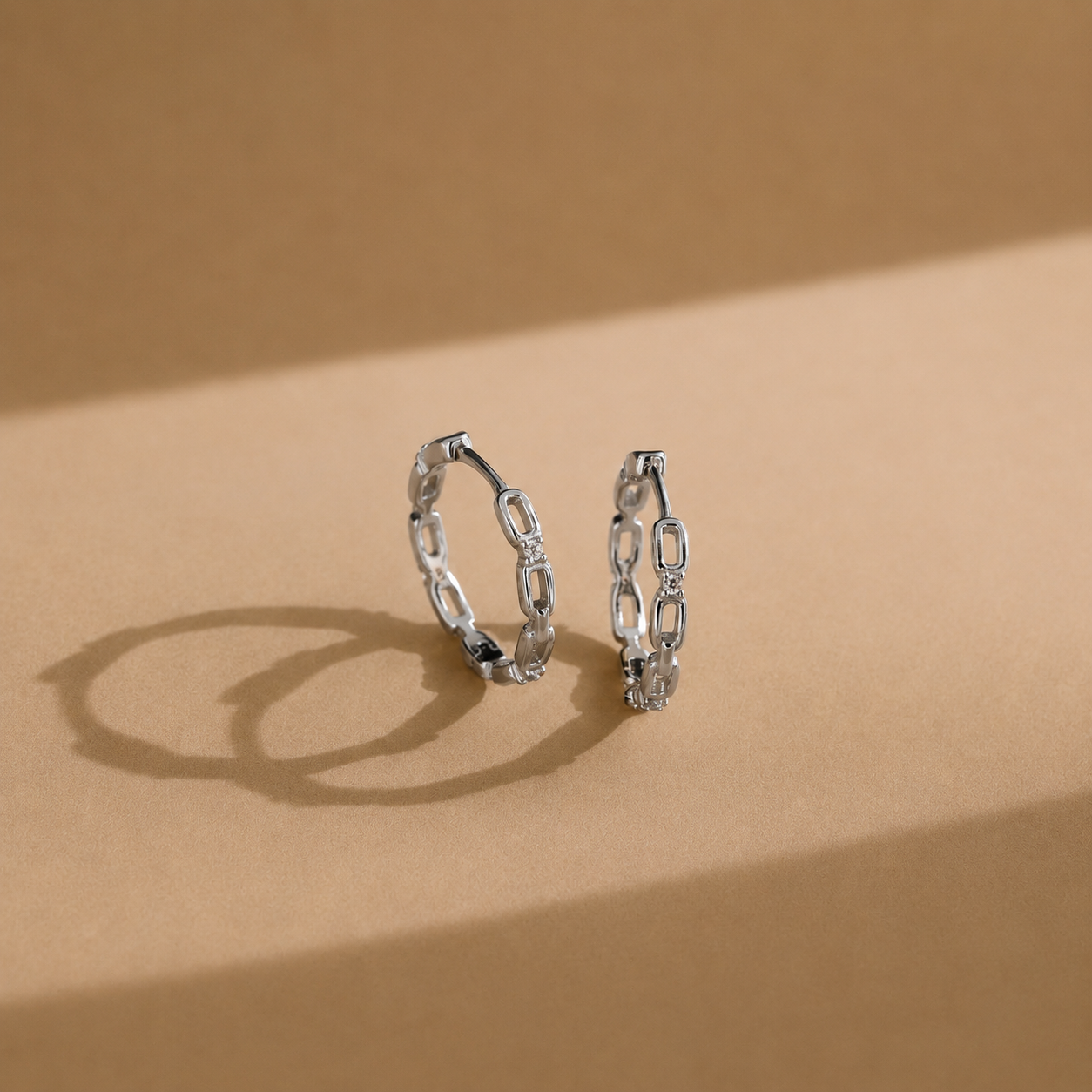 Pair of silver chain-link hoop earrings on a beige background